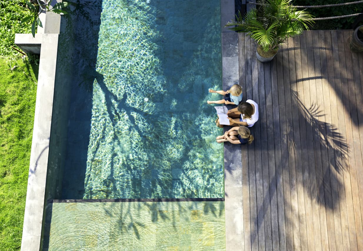 Two children and parent reading together by swimming pool. 