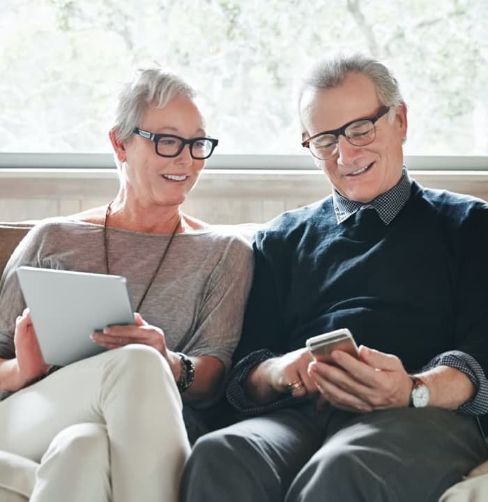 Senior couple sitting on couch and smiling at mobile devices.