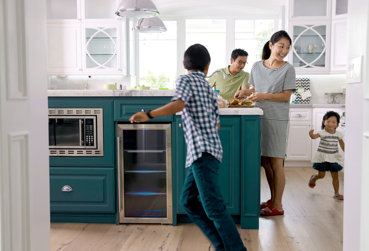 Children running through kitchen with parents smiling at them.