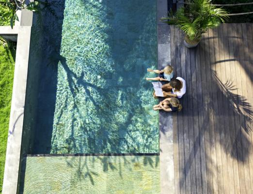 Two children and parent reading together by swimming pool. 