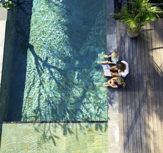 Two children and parent reading together by swimming pool. 